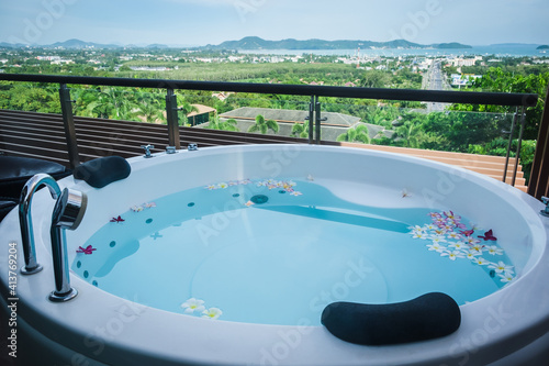 Bathtub outside at the balcony with tropical flowers in luxury hotel.