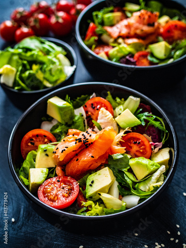 Salmon salad - smoked salmon with avocado and mix of vegetables on black wooden table 