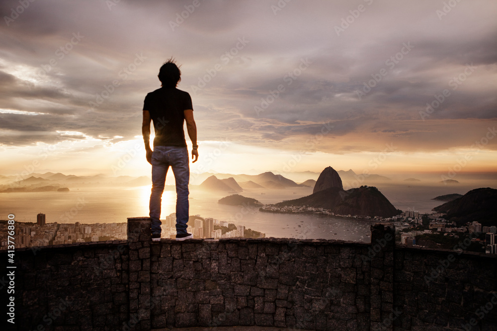 Rear view of silhouette man standing on retaining wall at observation point during sunset Rear view of silhouette man standing on retaining wall at observation point during sunset
