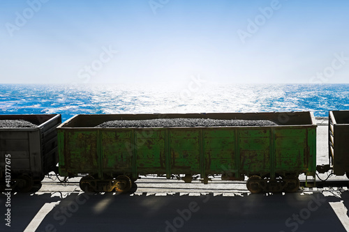 Industrial background. Coal in railway freight wagons, railroad on sea background