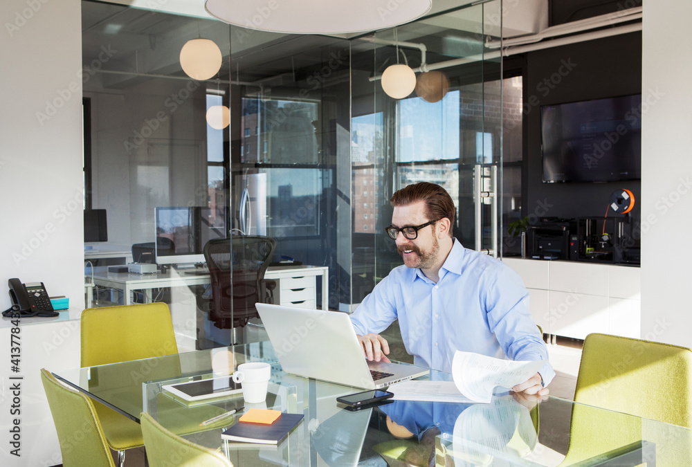 Happy businessman using laptop at conference table in board room Happy businessman using laptop at conference table in board room