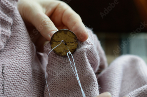 female workers' hands sew a wooden button to a jacket. close-up.