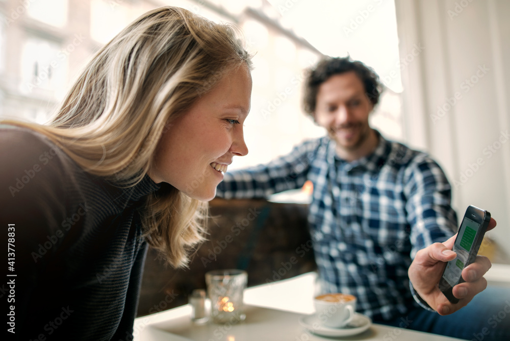 Man showing smart phone to woman in coffee shop Man showing smart phone to woman in coffee shop