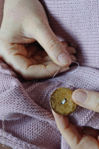 female workers' hands sew a wooden button to a jacket. close-up.