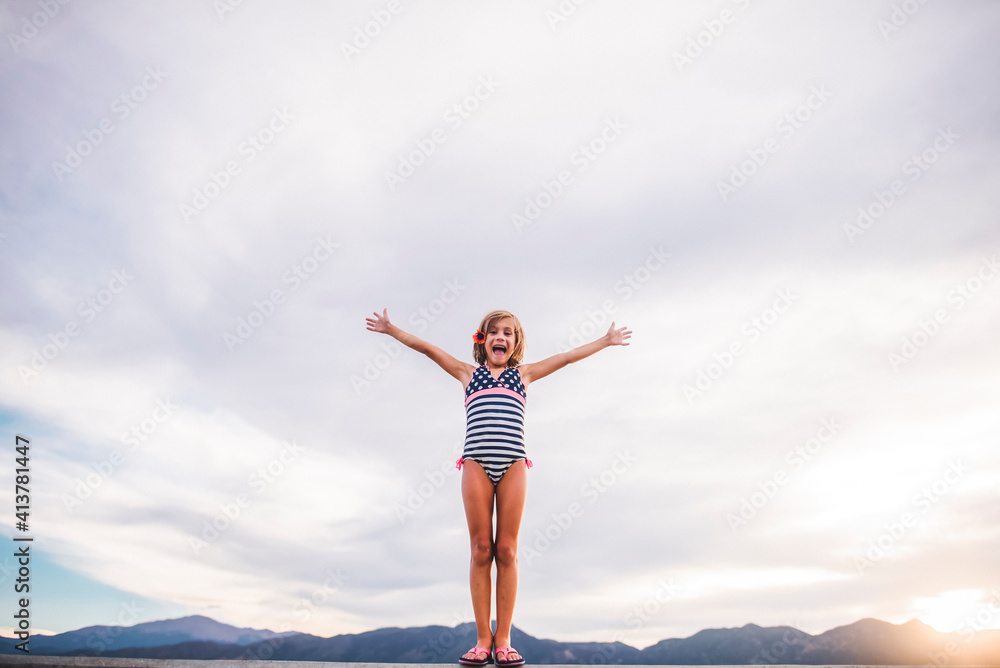 Low angle view of girl with arms outstretched wearing swimwear while standing against cloudy sky Low angle view of girl with arms outstretched wearing swimwear while standing against cloudy sky