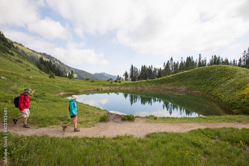 Side view of friends hiking on field by lake against cloudy sky Side view of friends hiking on field by lake against cloudy sky