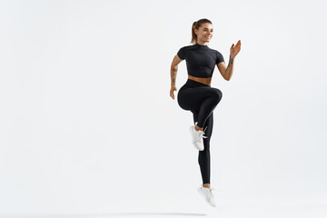 Healthy sport woman with fit body raising leg, jumping and exercising on white background. Female athelte in sportswear doing training workout for endurance