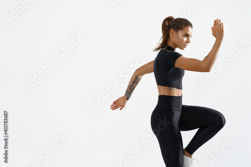 Determined muscular female athlete workout, raising leg and doing stretching exercises. Sport woman in sportswear training indoors, doing fitness aerobics, white background