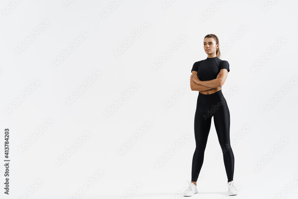 Determined sports woman in sport clothing standing on white background with crossed arms. Confident fitness female looking away, training and exercising concept Determined sports woman in sport clothing standing on white background with crossed arms. Confident fitness female looking away, training and exercising concept