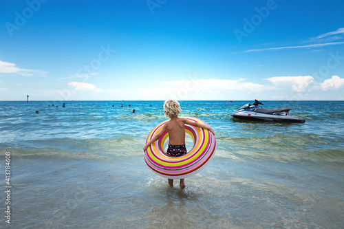 Rear view of boy carrying inner tube while walking towards sea