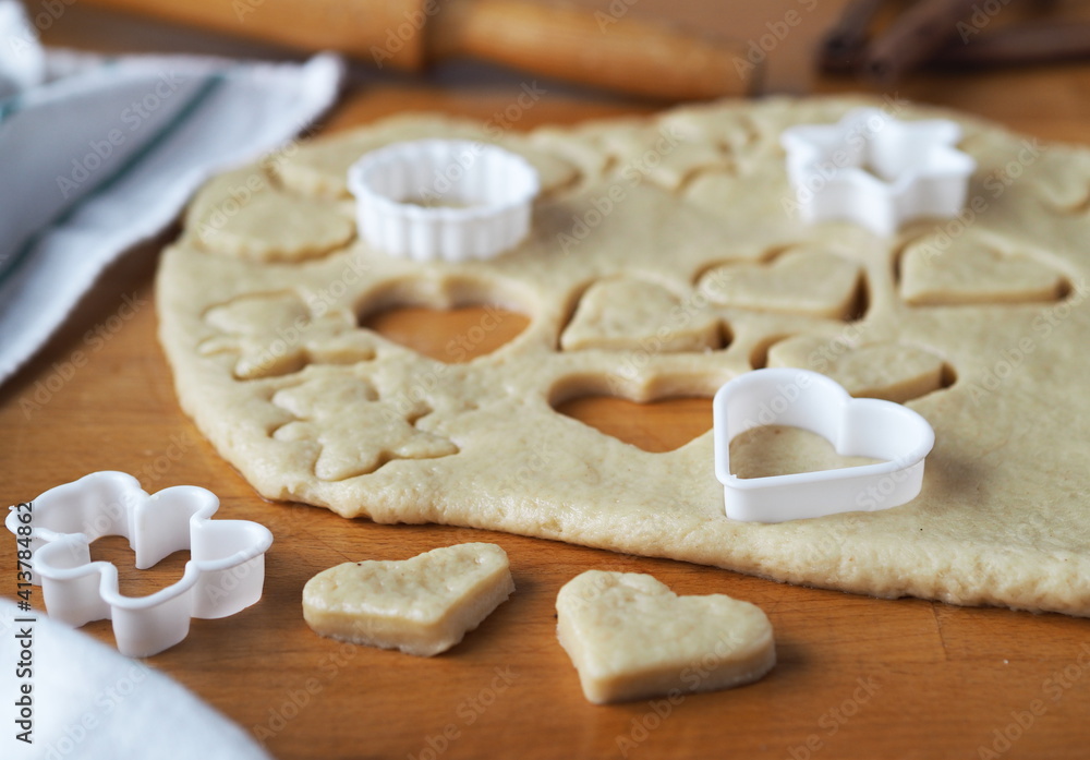 Raw shortbread cookies cut from a layer of dough with cookie cutters on a kitchen board on a dark wooden table.Confectionery background. Raw shortbread cookies cut from a layer of dough with cookie cutters on a kitchen board on a dark wooden table.Confectionery background.