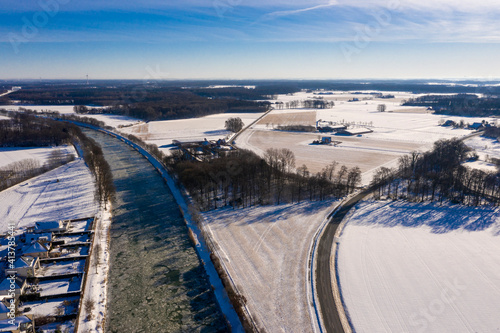 Wasserkanal in einer Stadt eingefroren im Winter bei eisigen minus Temperaturen in Deutschland. Luftaufnahmen beim sonnigen Tag im Februar über eingefrorene Straßen und Ackerbau.
