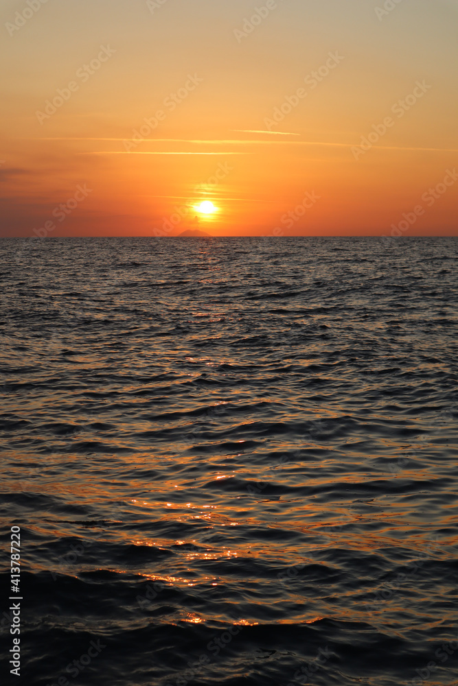 Obraz premium Seascape orange sunset and silhouette of Stromboli volcano in the haze on the horizon, Calabria, Italy