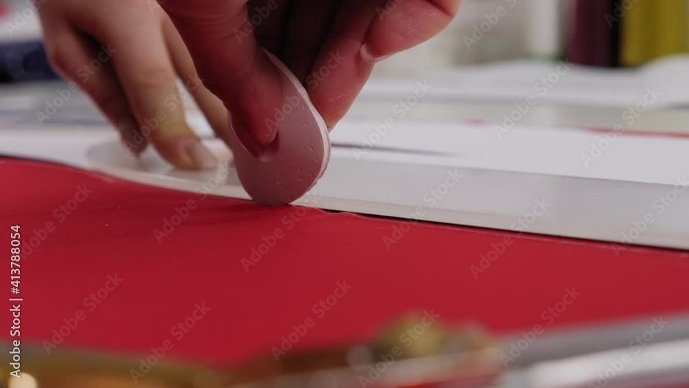 Close-up of woman hands making chalk markings of paper patterns on red fabric. The process of sewing an evening dress in a sewing workshop. Close-up of woman hands making chalk markings of paper patterns on red fabric. The process of sewing an evening dress in a sewing workshop.