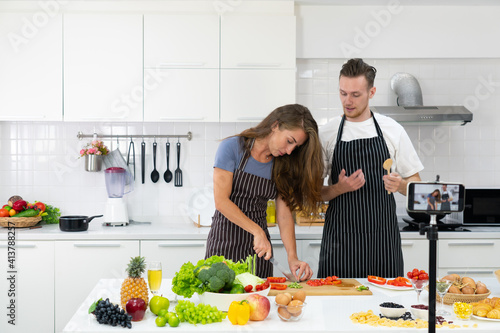 young caucasian couple who are blogger teaching people to cook healthy food via smartphone camera. family together concept