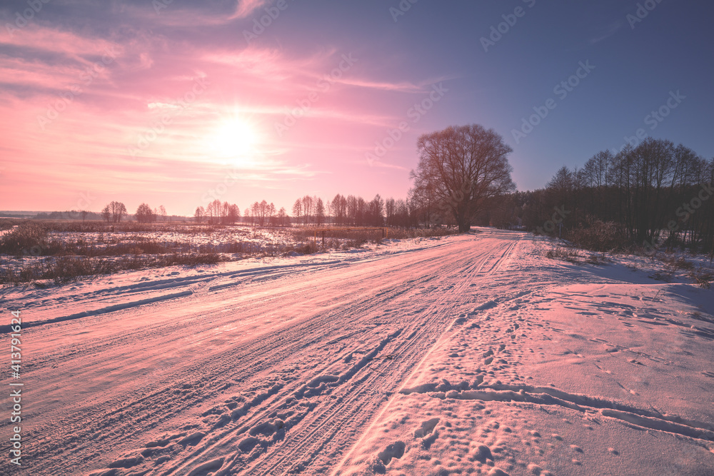 Rural winter landscape at sunrise. Country road covered with snow