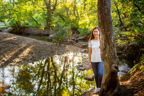 A teenage girl walks by a sunlit creek in the woods photo