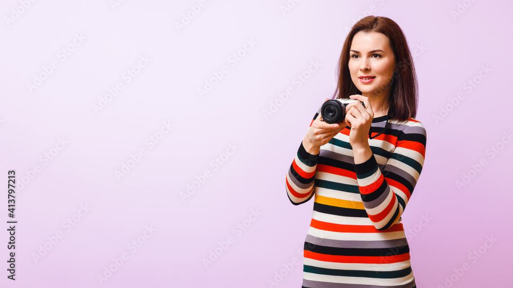 attractive young woman with a camera in her hands in a multicolored dress looks to the side on a pink background attractive young woman with a camera in her hands in a multicolored dress looks to the side on a pink background