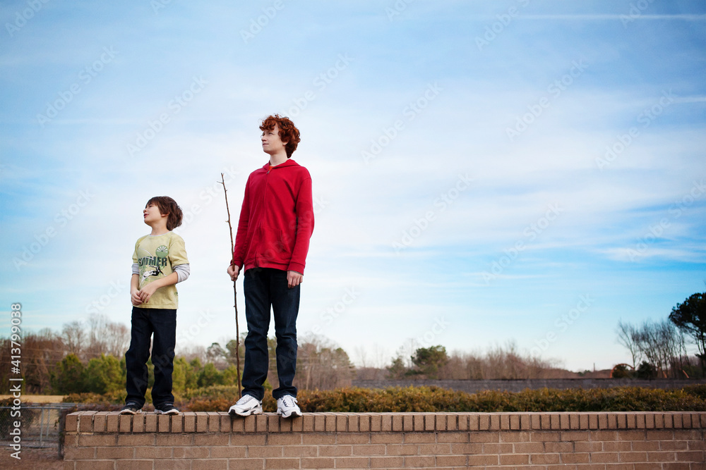Brothers standing on retaining wall against sky Brothers standing on retaining wall against sky
