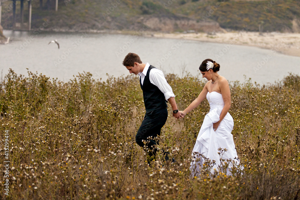 Newlywed couple holding hands while walking on grassy field Newlywed couple holding hands while walking on grassy field