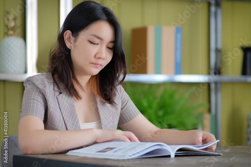 Young Asian woman sitting at the table and reading a book in a library.