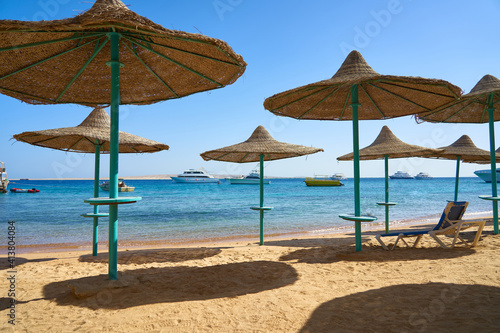 Beach with clean white sand on a sunny day. Umbrellas and sun lounger on the seashore against the blue sky