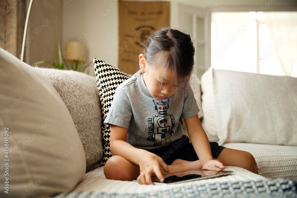 Curious girl using tablet computer while sitting on sofa at home Curious girl using tablet computer while sitting on sofa at home