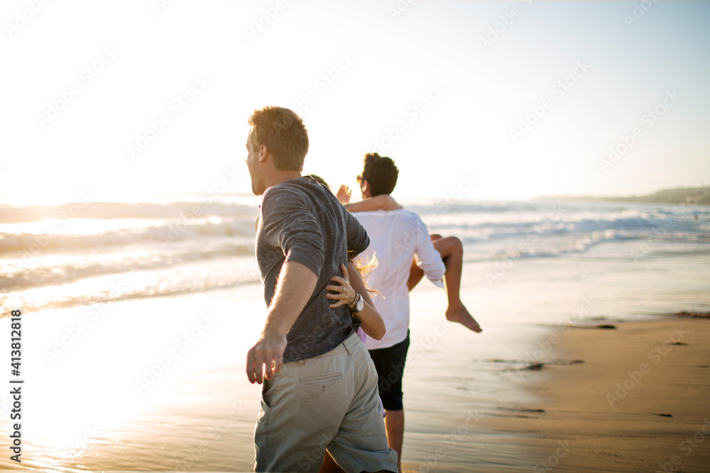 Rear view of couples running on beach against clear sky Rear view of couples running on beach against clear sky