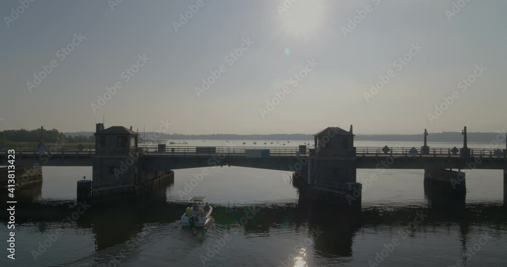 Sun Shining on Cars Driving on Small Bridge while Speedboat Passes Under Sun Shining on Cars Driving on Small Bridge while Speedboat Passes Under