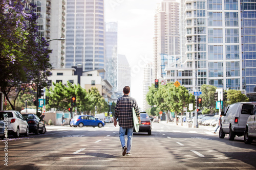 Wallpaper Mural Rear view of man holding surfboard and walking on city street Torontodigital.ca