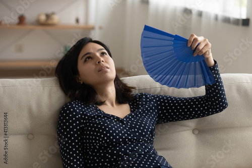 Obraz na plátně Exhausted young asian woman recline on couch suffer from extreme heat unhappy to live in apartment without air conditioner