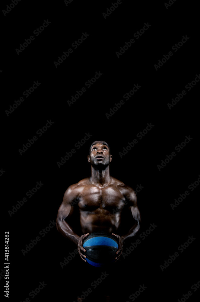 Muscular man holding ball while standing against black background Muscular man holding ball while standing against black background