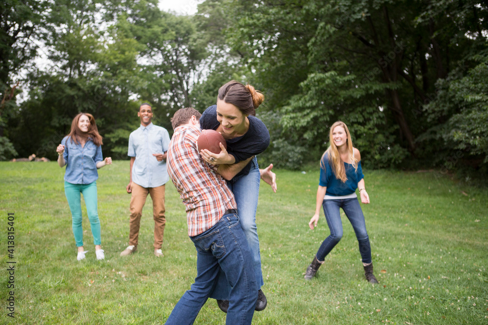 Man defending woman holding football ball while friends watching them on field Man defending woman holding football ball while friends watching them on field