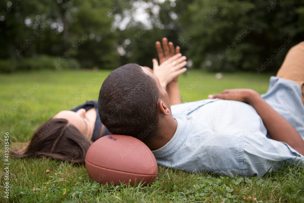 Man resting head on football ball while lying with woman on field Man resting head on football ball while lying with woman on field