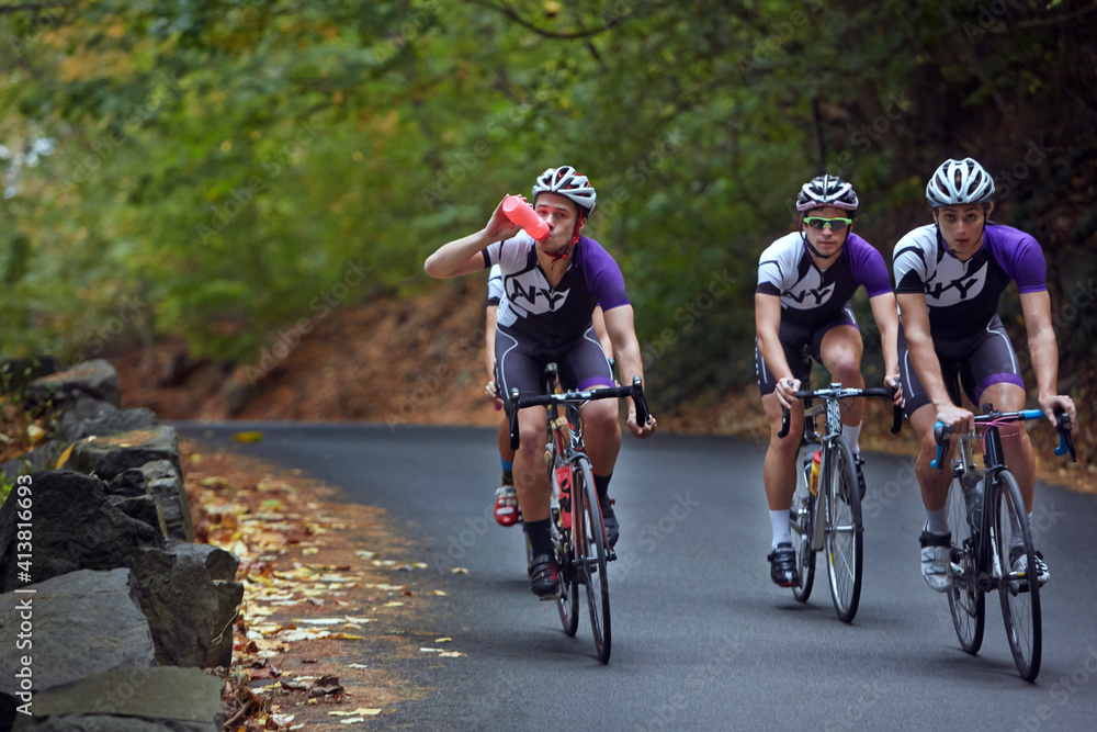 Male athlete drinking water while riding bicycle with friends Male athlete drinking water while riding bicycle with friends