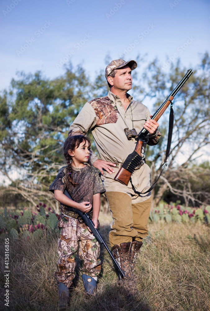 Hunters holding rifle and looking away while standing on grassy field
