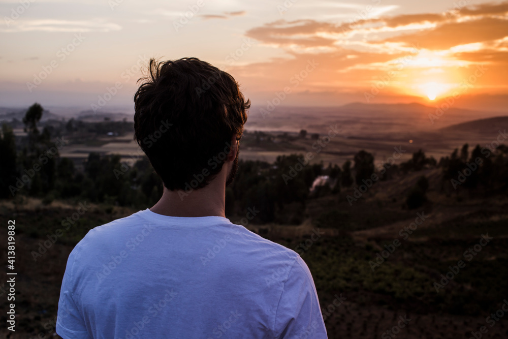 Rear view of man looking at view while standing on mountain against sky during sunset Rear view of man looking at view while standing on mountain against sky during sunset