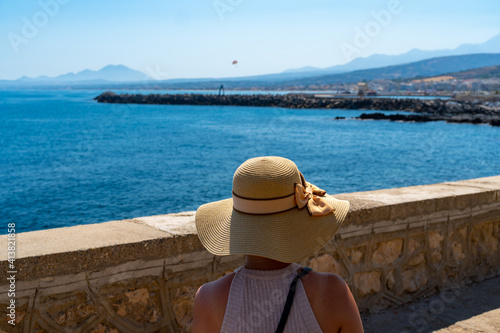 Girl with a hat sitting on bench. Bastion of the sea fortress in Rethymnon, Crete, Greece. Selective focus