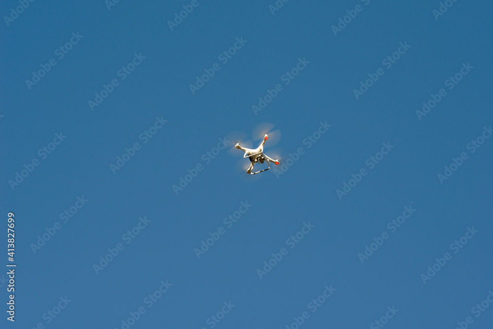 Low angle view of quadcopter flying against clear blue sky during sunny day Low angle view of quadcopter flying against clear blue sky during sunny day