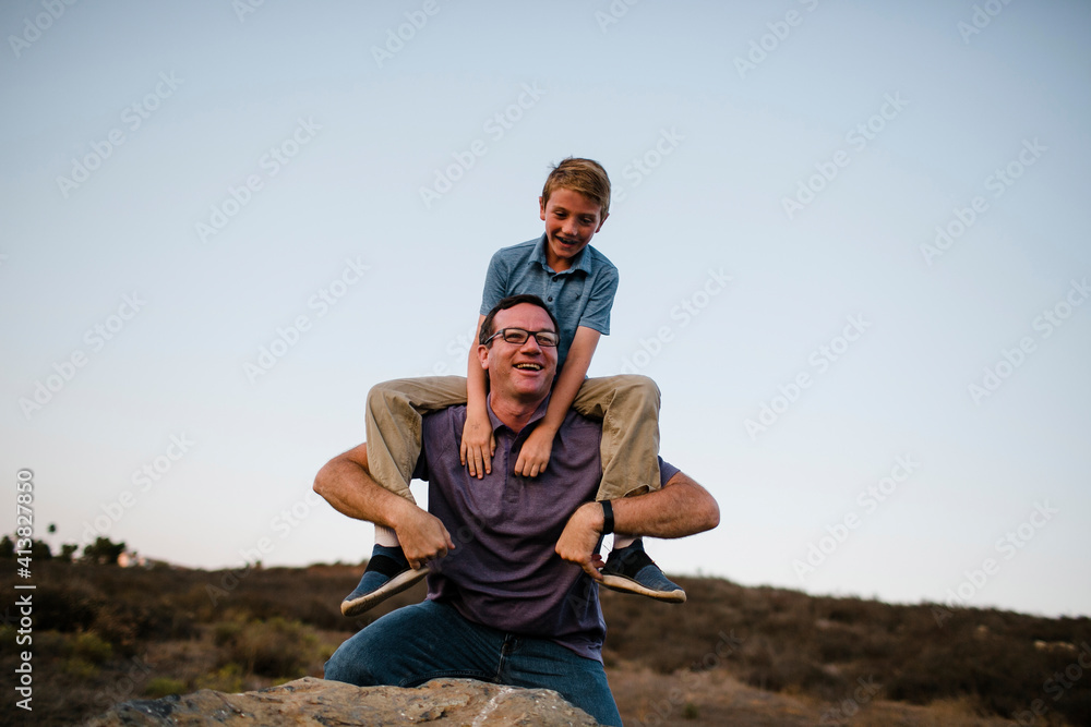 Playful father carrying son on shoulders against clear sky Playful father carrying son on shoulders against clear sky