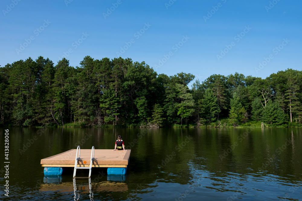 Rear view of boy sitting on floating platform in lake at forest Rear view of boy sitting on floating platform in lake at forest