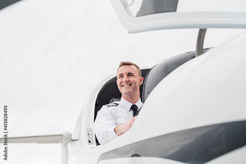 Low angle view of smiling male pilot sitting in airplane against sky at airport Low angle view of smiling male pilot sitting in airplane against sky at airport