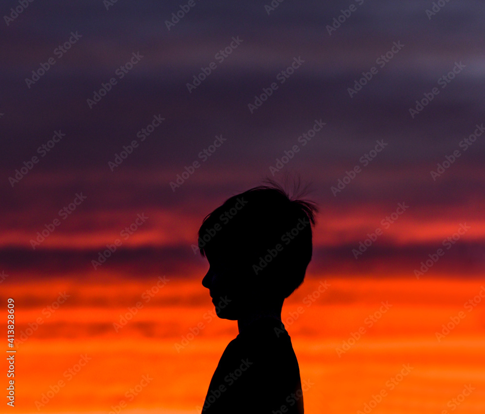 Side view of silhouette boy standing against dramatic sky in sunset Side view of silhouette boy standing against dramatic sky in sunset