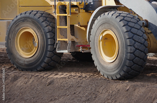 Close-up partial view of a yellow heavy equipment earth mover vehicle on a street construction site