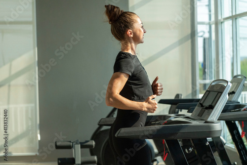 beautiful woman in sportswear running on a treadmill in a sports club gym © Supavadee