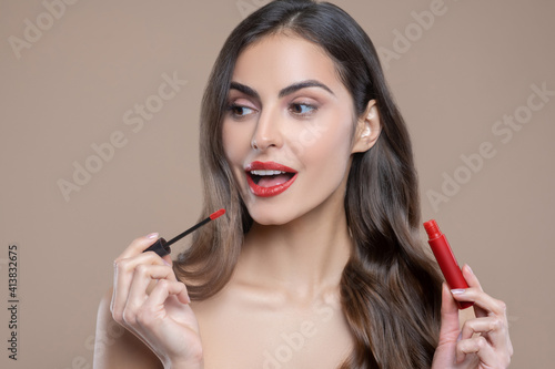 Long-haired woman painting lips with red gloss