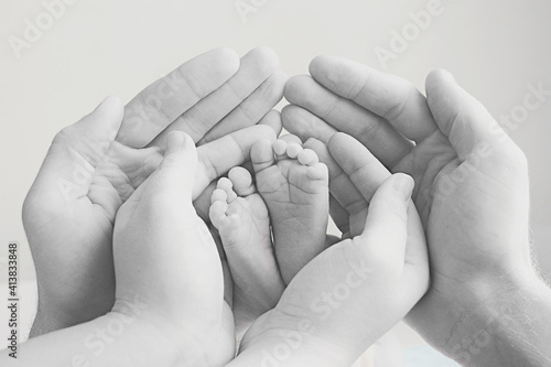 mother and father gently hold the baby's foot in their hands. Black and white image with soft focus on the baby's leg