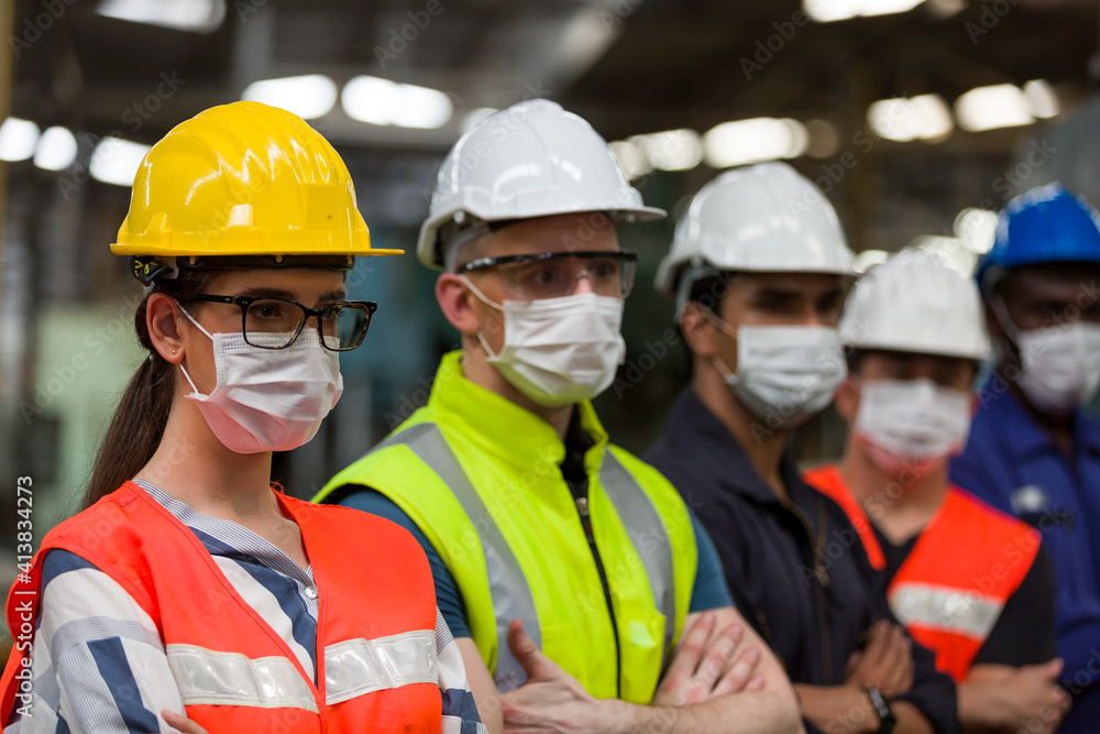 Group of diversity factory worker wearing face mask working at factory. Team of technician worker in safety uniform, helmet and face mask in the industry factory. Industry and health care concept Group of diversity factory worker wearing face mask working at factory. Team of technician worker in safety uniform, helmet and face mask in the industry factory. Industry and health care concept