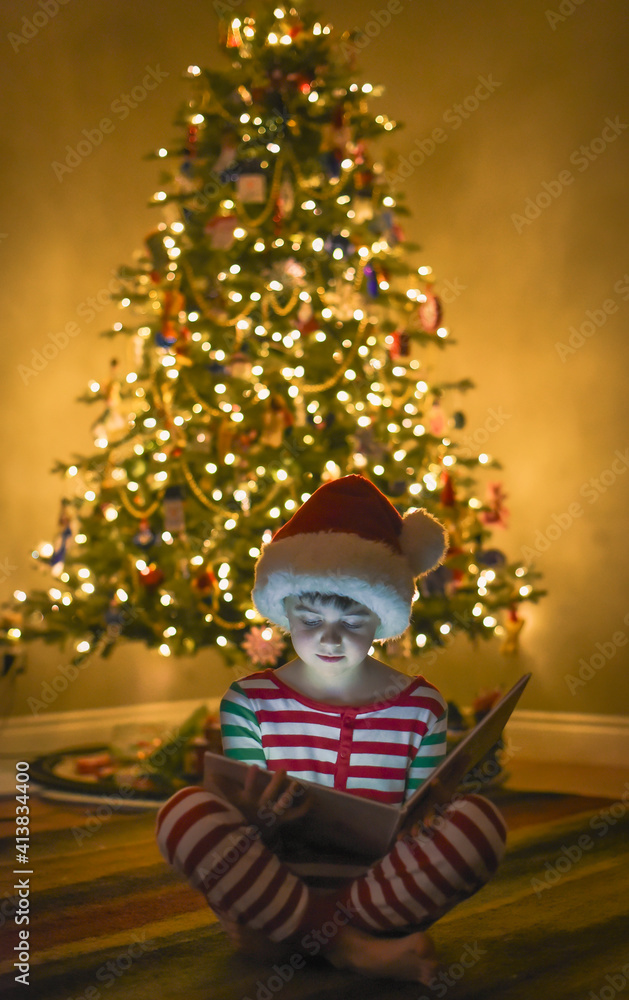 Boy reading book in front of Christmas tree with face illuminated. Boy reading book in front of Christmas tree with face illuminated.