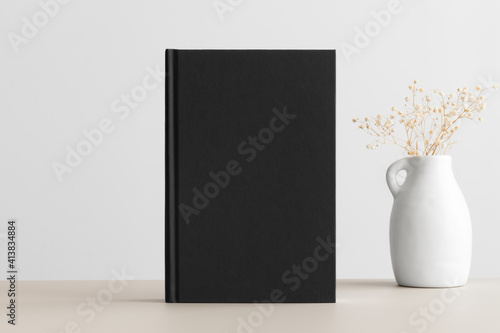 Black book mockup with a gypsophila decoration on the beige table. photo